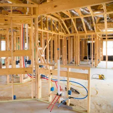 Close-up view of the interior structure of a house under construction, showing detailed wooden wall framing, electrical wiring conduits, and plumbing installation by Best Construction LA.